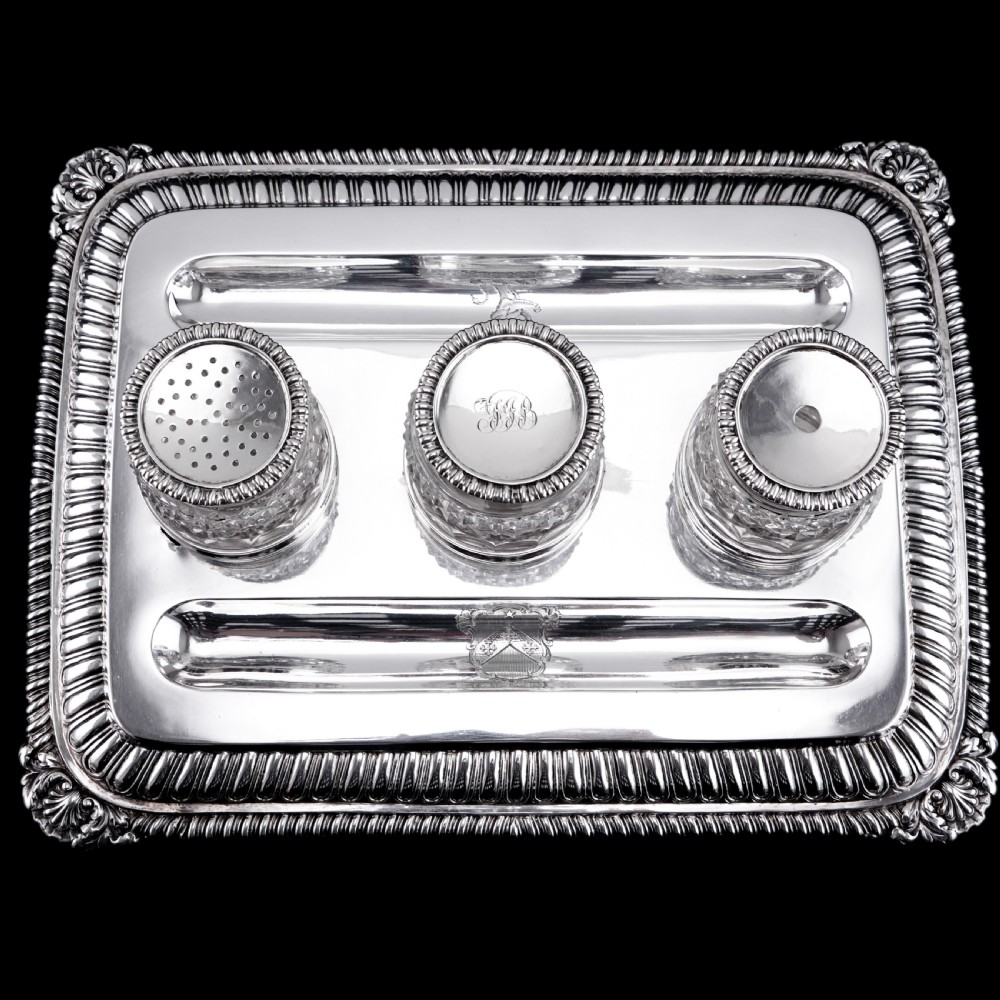A rectangular Regency sterling silver inkstand featuring gadrooned borders, shell corners, two pen depressions, and three cut glass pots with silver lids.