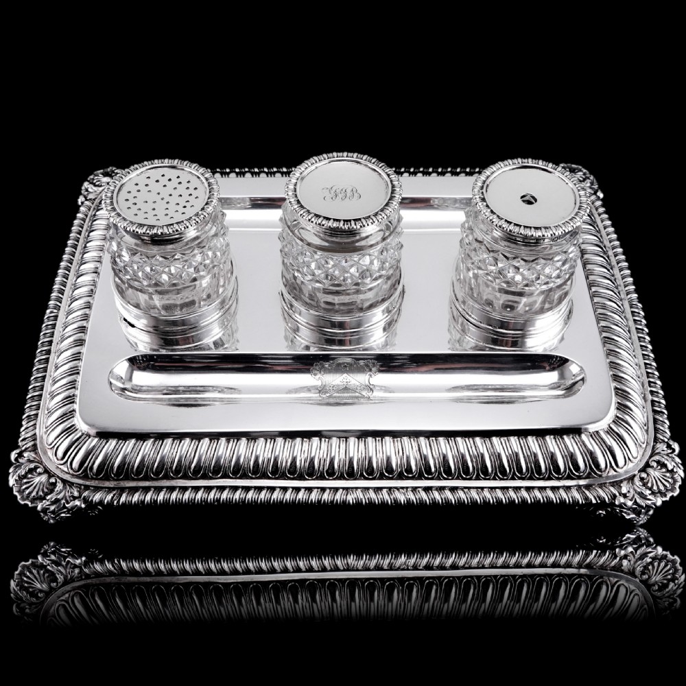 A rectangular Regency sterling silver inkstand featuring gadrooned borders, shell corners, two pen depressions, and three cut glass pots with silver lids. View II
