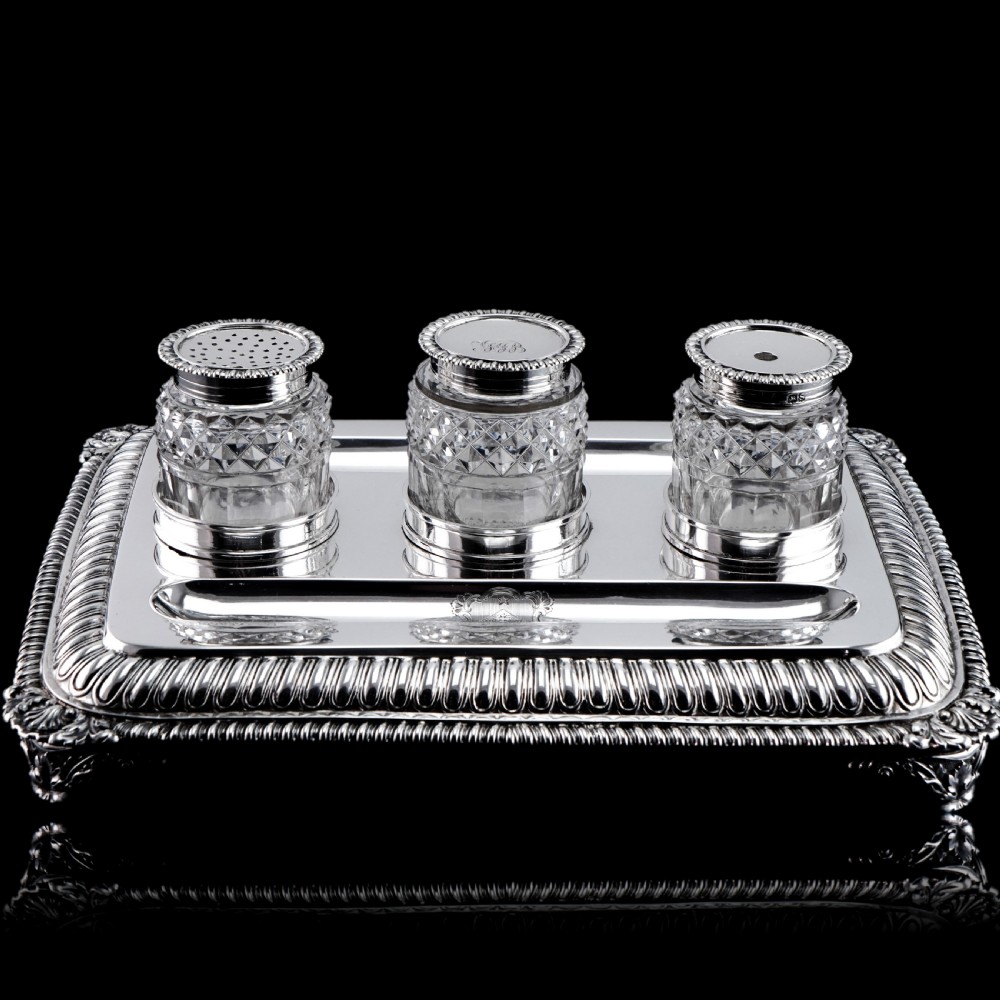 A rectangular Regency sterling silver inkstand featuring gadrooned borders, shell corners, two pen depressions, and three cut glass pots with silver lids. View VI