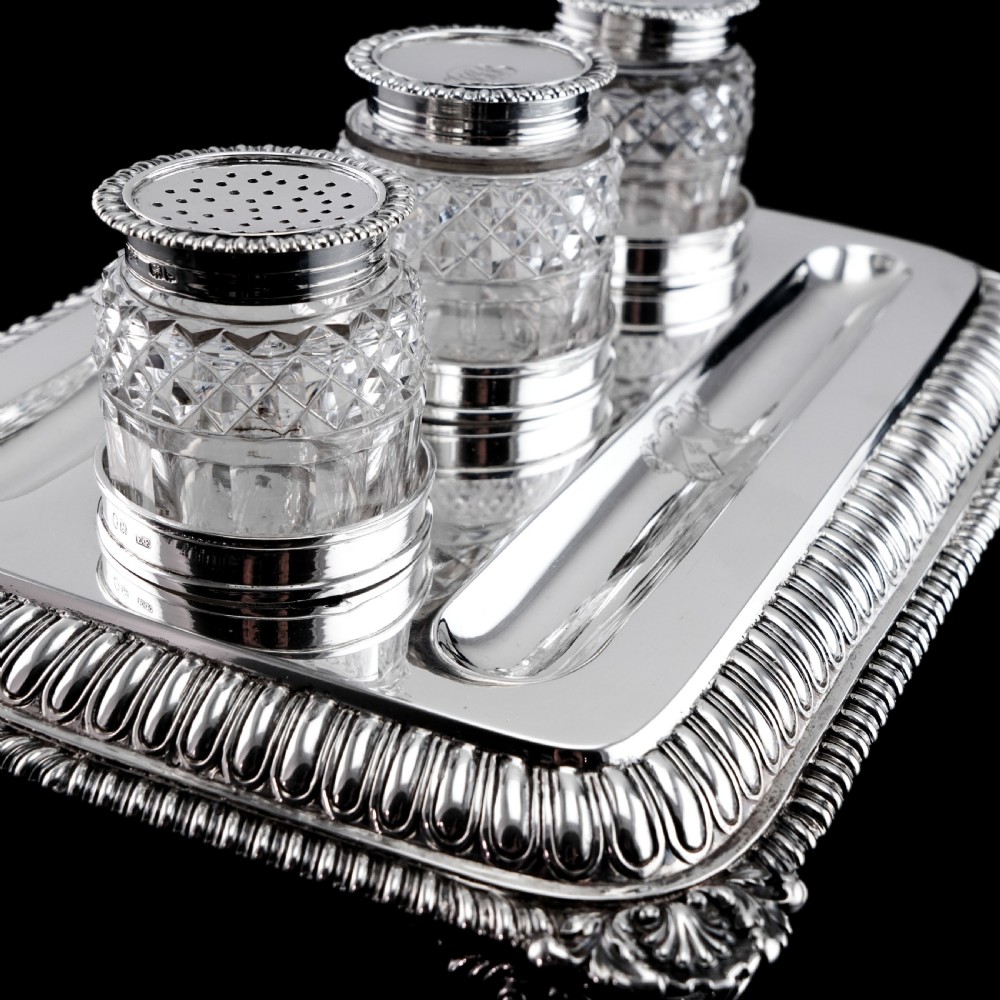 A rectangular Regency sterling silver inkstand featuring gadrooned borders, shell corners, two pen depressions, and three cut glass pots with silver lids. View X