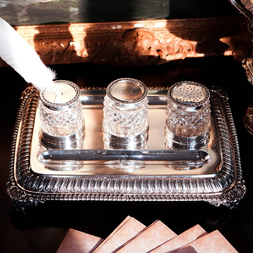 A rectangular Regency sterling silver inkstand featuring gadrooned borders, shell corners, two pen depressions, and three cut glass pots with silver lids. View XV