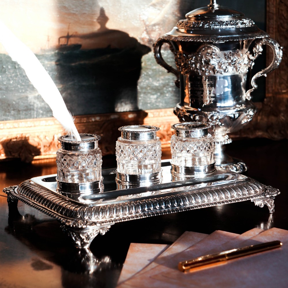 A rectangular Regency sterling silver inkstand featuring gadrooned borders, shell corners, two pen depressions, and three cut glass pots with silver lids. View XVI
