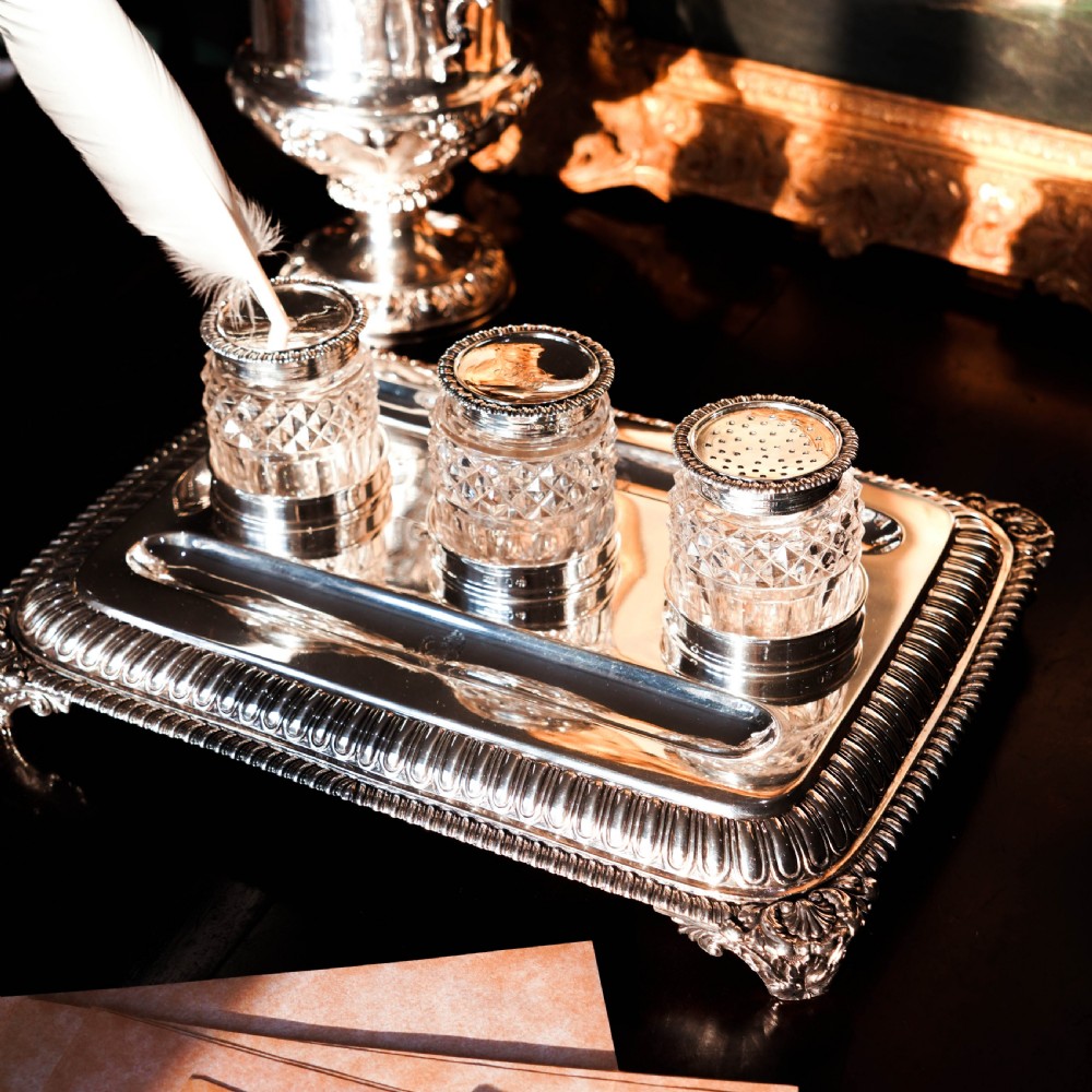 A rectangular Regency sterling silver inkstand featuring gadrooned borders, shell corners, two pen depressions, and three cut glass pots with silver lids. View XVII