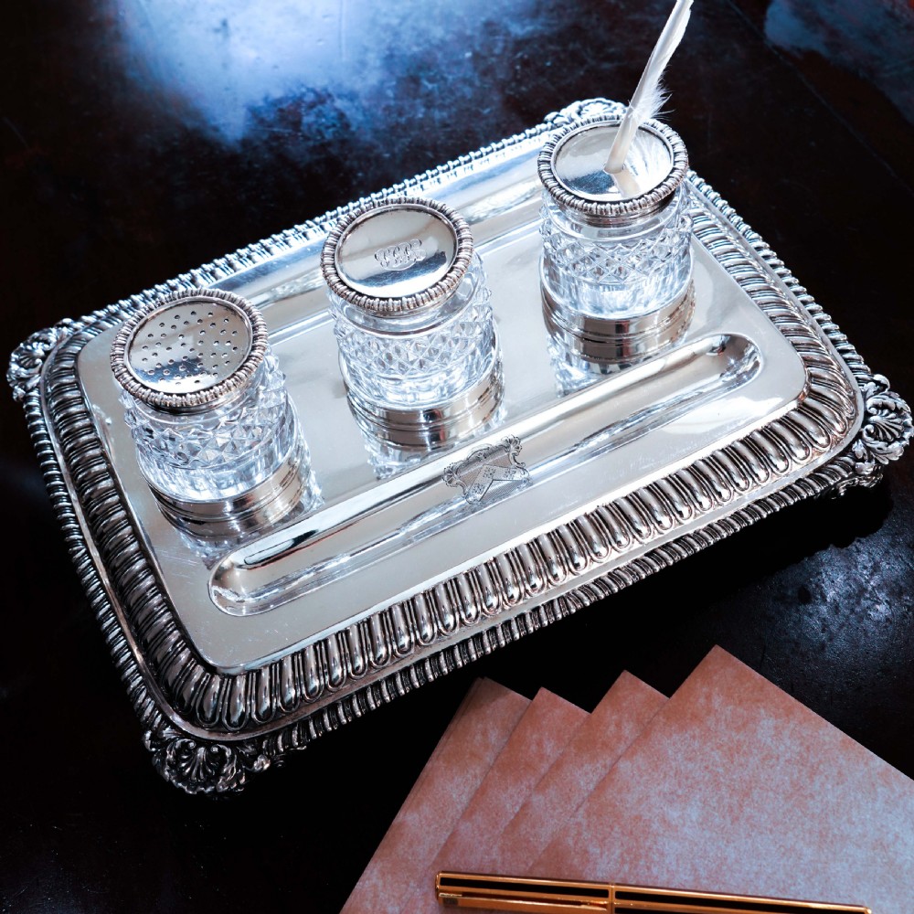 A rectangular Regency sterling silver inkstand featuring gadrooned borders, shell corners, two pen depressions, and three cut glass pots with silver lids. View XIX
