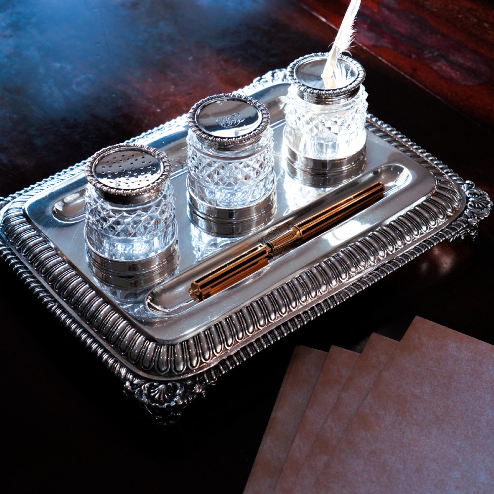 A rectangular Regency sterling silver inkstand featuring gadrooned borders, shell corners, two pen depressions, and three cut glass pots with silver lids. View XX