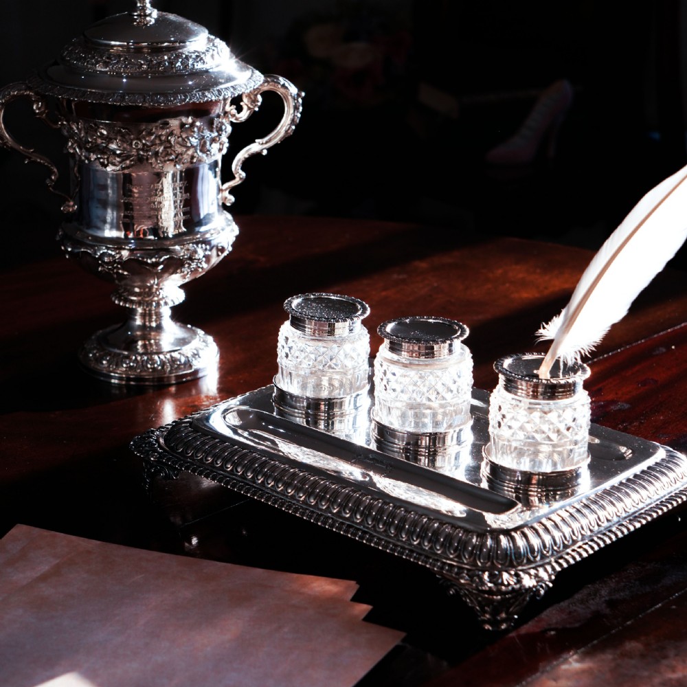 A rectangular Regency sterling silver inkstand featuring gadrooned borders, shell corners, two pen depressions, and three cut glass pots with silver lids. View XXII