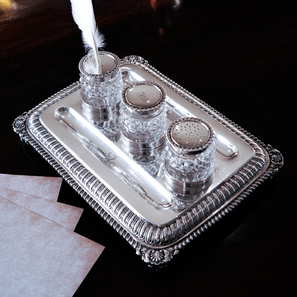 A rectangular Regency sterling silver inkstand featuring gadrooned borders, shell corners, two pen depressions, and three cut glass pots with silver lids. View XXIV