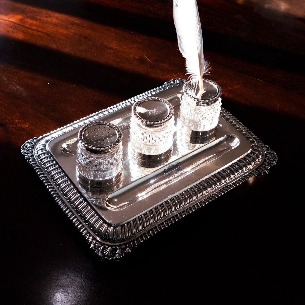 A rectangular Regency sterling silver inkstand featuring gadrooned borders, shell corners, two pen depressions, and three cut glass pots with silver lids. View XXVI