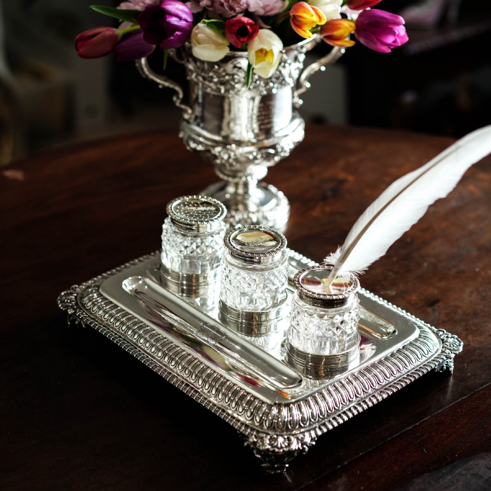 A rectangular Regency sterling silver inkstand featuring gadrooned borders, shell corners, two pen depressions, and three cut glass pots with silver lids. View XXX