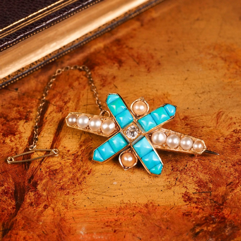 An antique Victorian gold cross-shaped brooch set with cabochon turquoise, white seed pearls, a central diamond, and attached to a safety chain. View VII