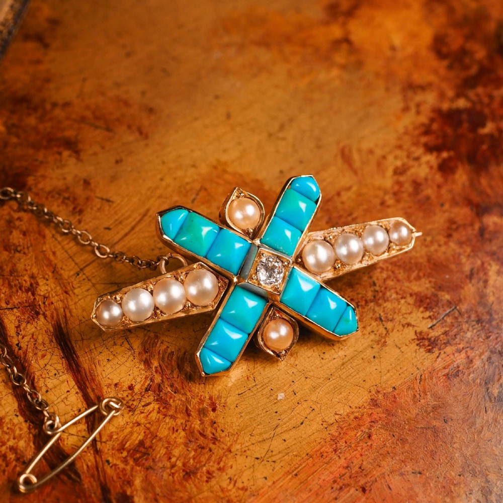 An antique Victorian gold cross-shaped brooch set with cabochon turquoise, white seed pearls, a central diamond, and attached to a safety chain. View II
