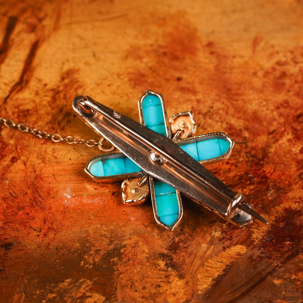 An antique Victorian gold cross-shaped brooch set with cabochon turquoise, white seed pearls, a central diamond, and attached to a safety chain. View III