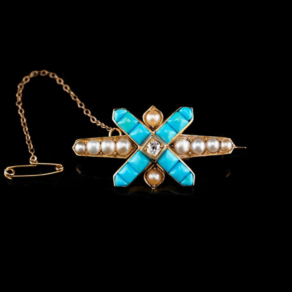 An antique Victorian gold cross-shaped brooch set with cabochon turquoise, white seed pearls, a central diamond, and attached to a safety chain. View IV