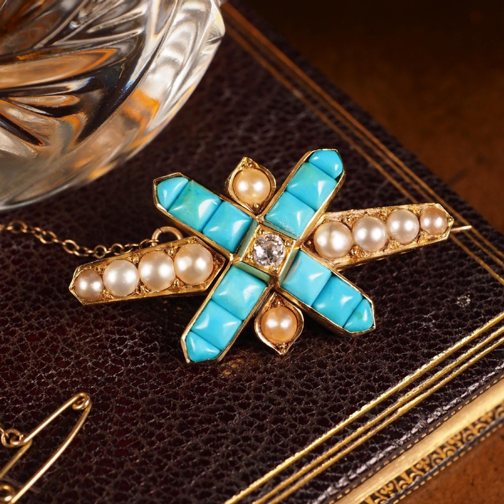 An antique Victorian gold cross-shaped brooch set with cabochon turquoise, white seed pearls, a central diamond, and attached to a safety chain. View V