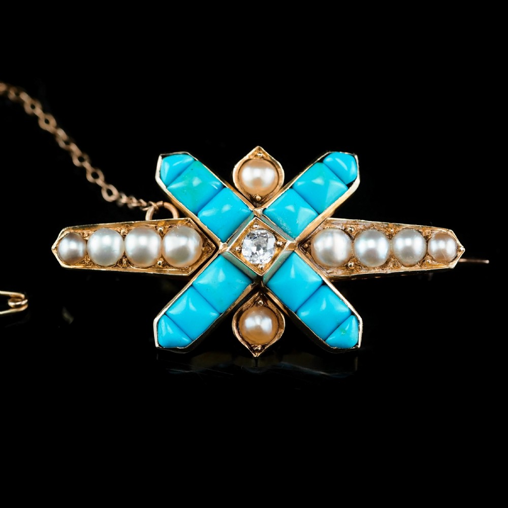 An antique Victorian gold cross-shaped brooch set with cabochon turquoise, white seed pearls, a central diamond, and attached to a safety chain. View VI