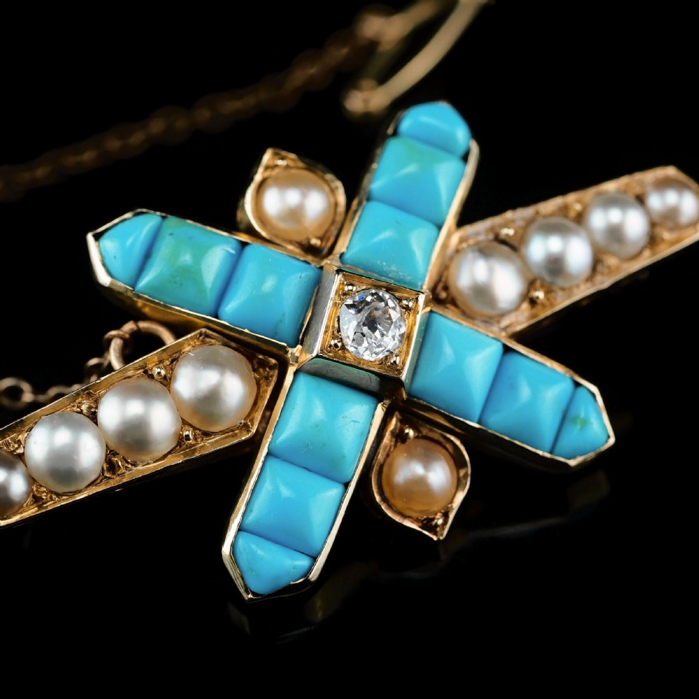 An antique Victorian gold cross-shaped brooch set with cabochon turquoise, white seed pearls, a central diamond, and attached to a safety chain. View IX