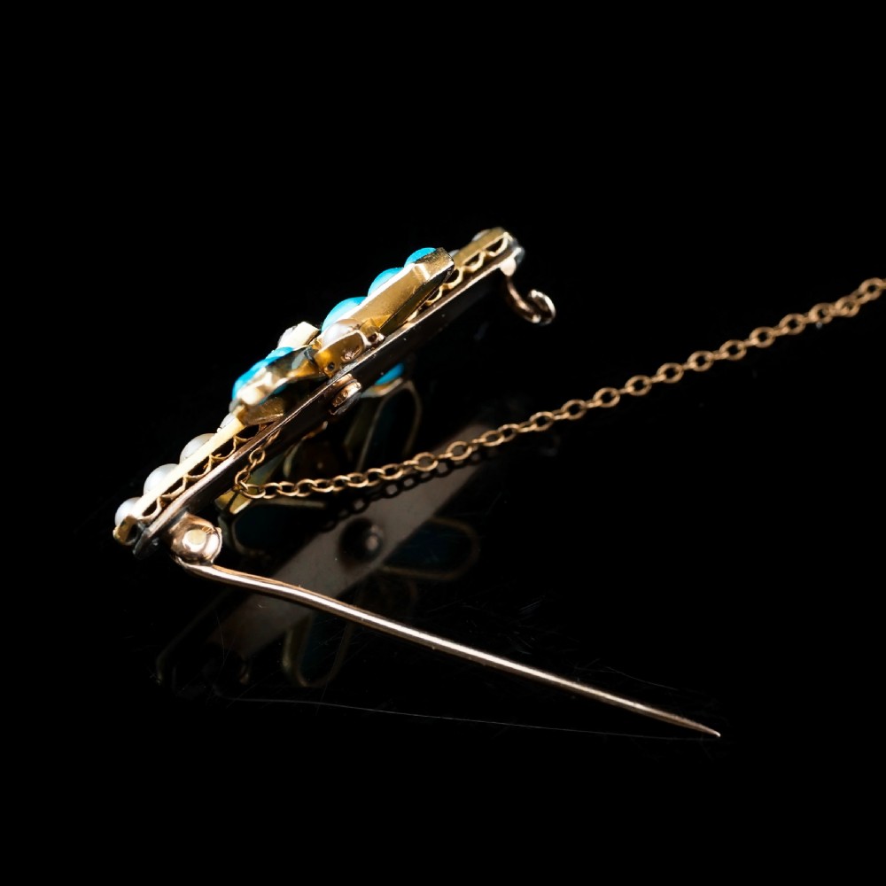 An antique Victorian gold cross-shaped brooch set with cabochon turquoise, white seed pearls, a central diamond, and attached to a safety chain. View XIV