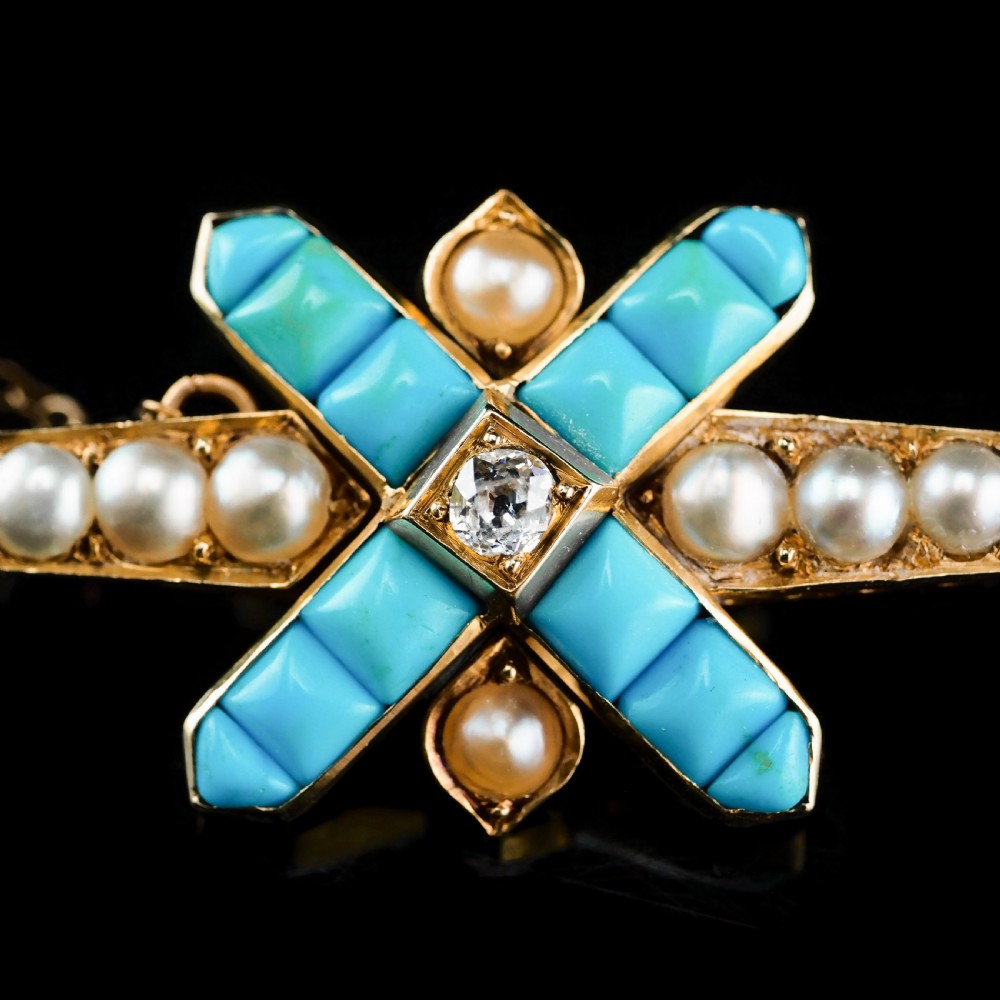 An antique Victorian gold cross-shaped brooch set with cabochon turquoise, white seed pearls, a central diamond, and attached to a safety chain. View XV