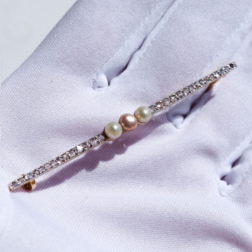 An antique 18ct gold and platinum bar brooch featuring three central pearls flanked by a row of small diamonds.