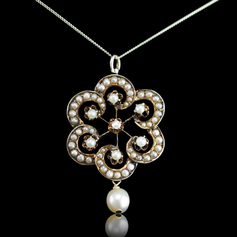 A Victorian 14ct yellow gold circular scrollwork pendant set with seed pearls, a central diamond, and an articulated pearl drop suspended from a fine chain.