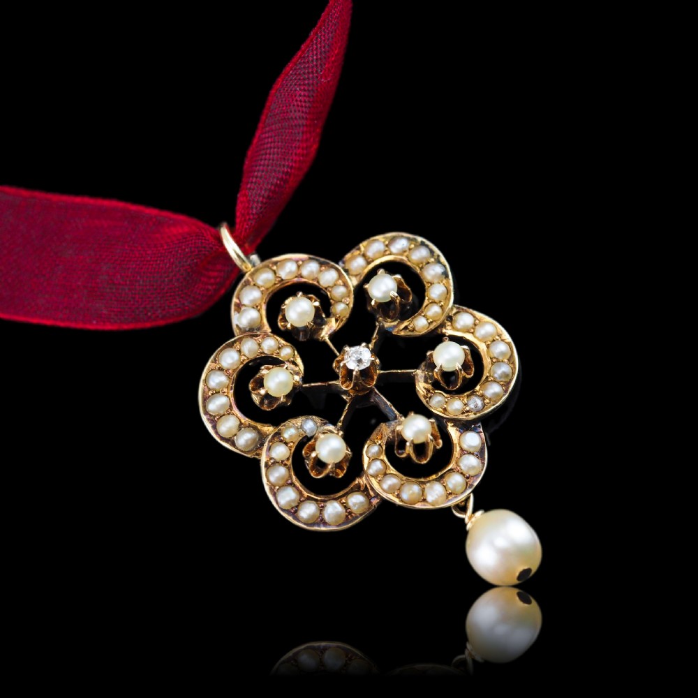 A Victorian 14ct yellow gold circular scrollwork pendant set with seed pearls, a central diamond, and an articulated pearl drop suspended from a fine chain. View V