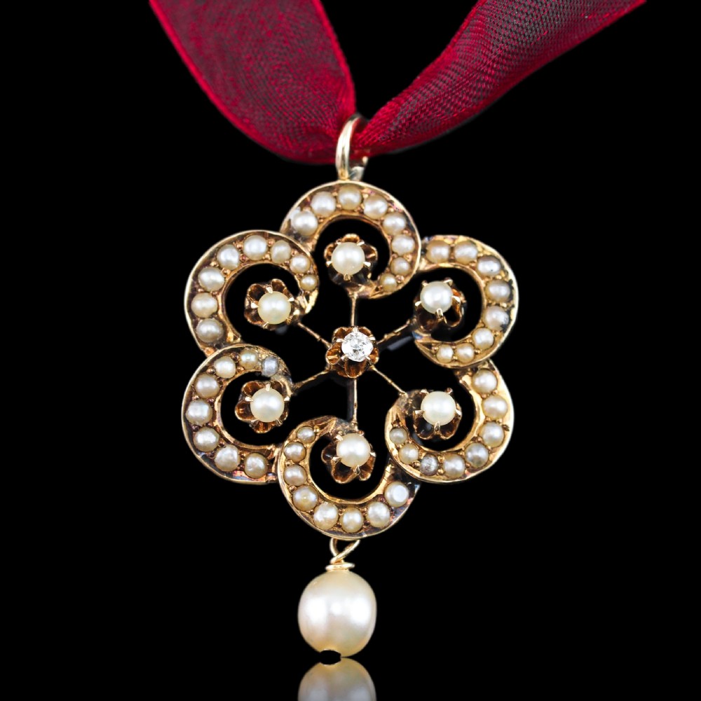 A Victorian 14ct yellow gold circular scrollwork pendant set with seed pearls, a central diamond, and an articulated pearl drop suspended from a fine chain. View VI
