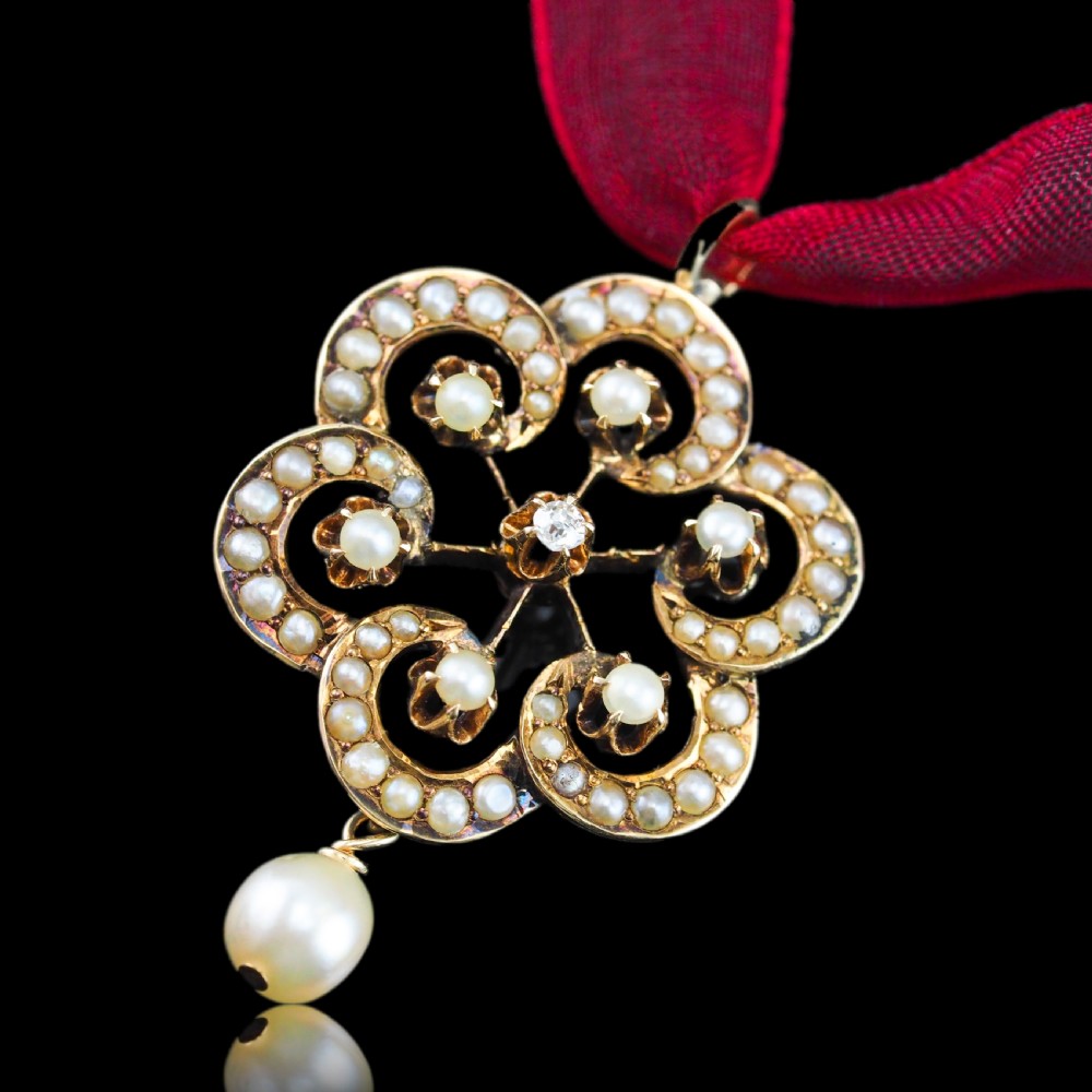 A Victorian 14ct yellow gold circular scrollwork pendant set with seed pearls, a central diamond, and an articulated pearl drop suspended from a fine chain. View VII