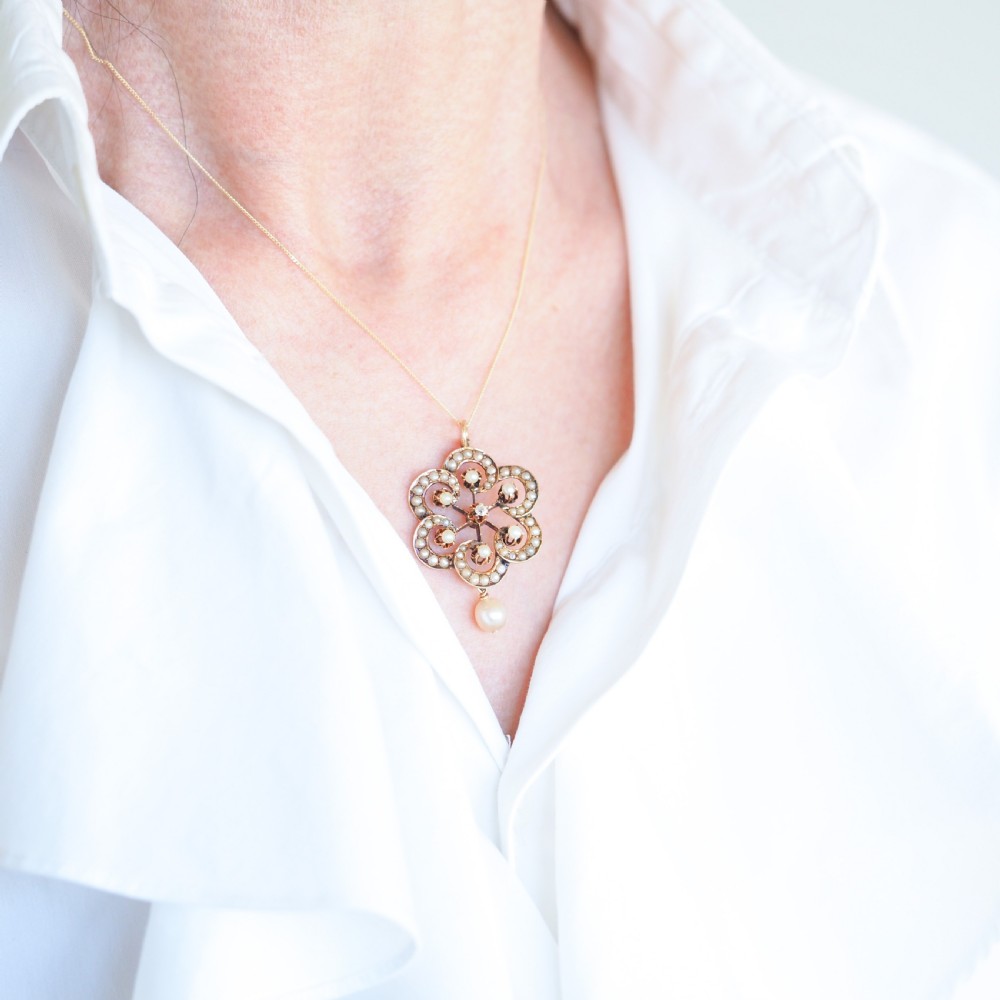 A Victorian 14ct yellow gold circular scrollwork pendant set with seed pearls, a central diamond, and an articulated pearl drop suspended from a fine chain. View VIII