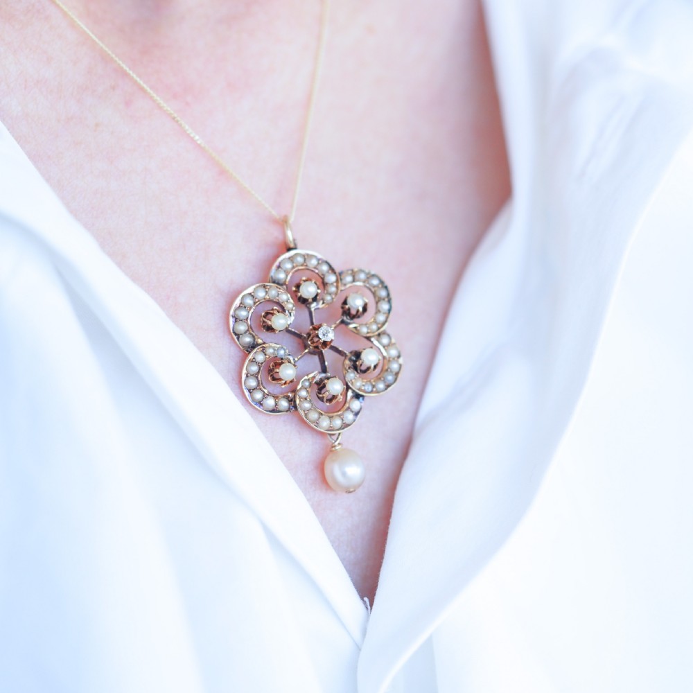 A Victorian 14ct yellow gold circular scrollwork pendant set with seed pearls, a central diamond, and an articulated pearl drop suspended from a fine chain. View IX