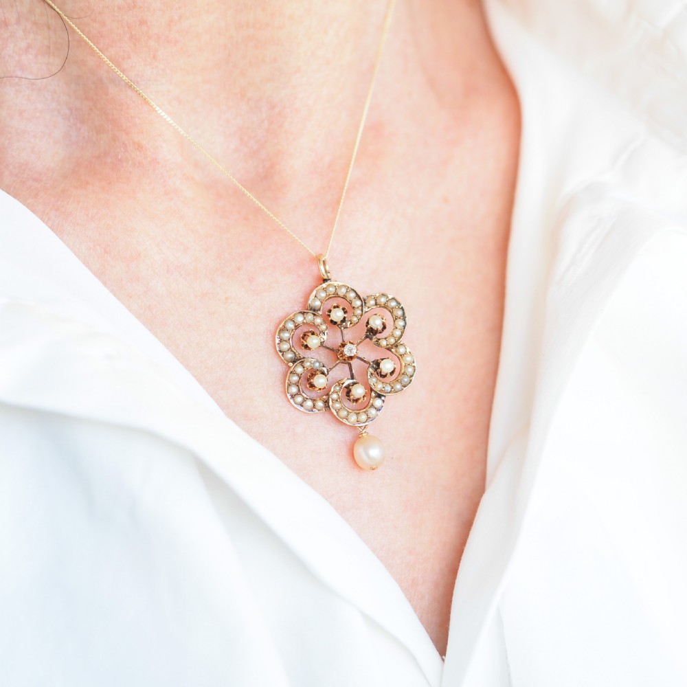 A Victorian 14ct yellow gold circular scrollwork pendant set with seed pearls, a central diamond, and an articulated pearl drop suspended from a fine chain. View X