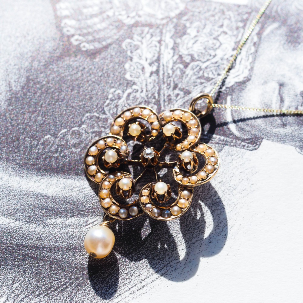 A Victorian 14ct yellow gold circular scrollwork pendant set with seed pearls, a central diamond, and an articulated pearl drop suspended from a fine chain. View XI
