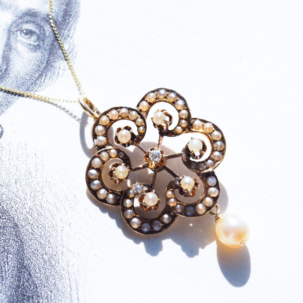 A Victorian 14ct yellow gold circular scrollwork pendant set with seed pearls, a central diamond, and an articulated pearl drop suspended from a fine chain. View XII