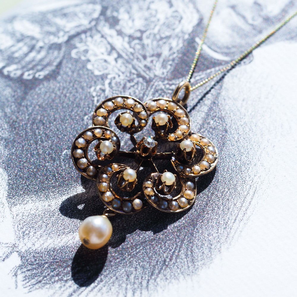 A Victorian 14ct yellow gold circular scrollwork pendant set with seed pearls, a central diamond, and an articulated pearl drop suspended from a fine chain. View XIII