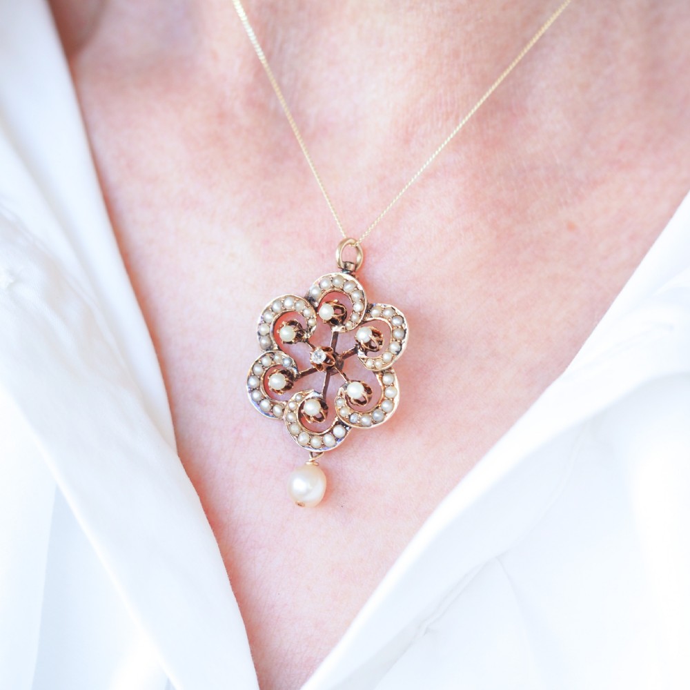 A Victorian 14ct yellow gold circular scrollwork pendant set with seed pearls, a central diamond, and an articulated pearl drop suspended from a fine chain. View XIV