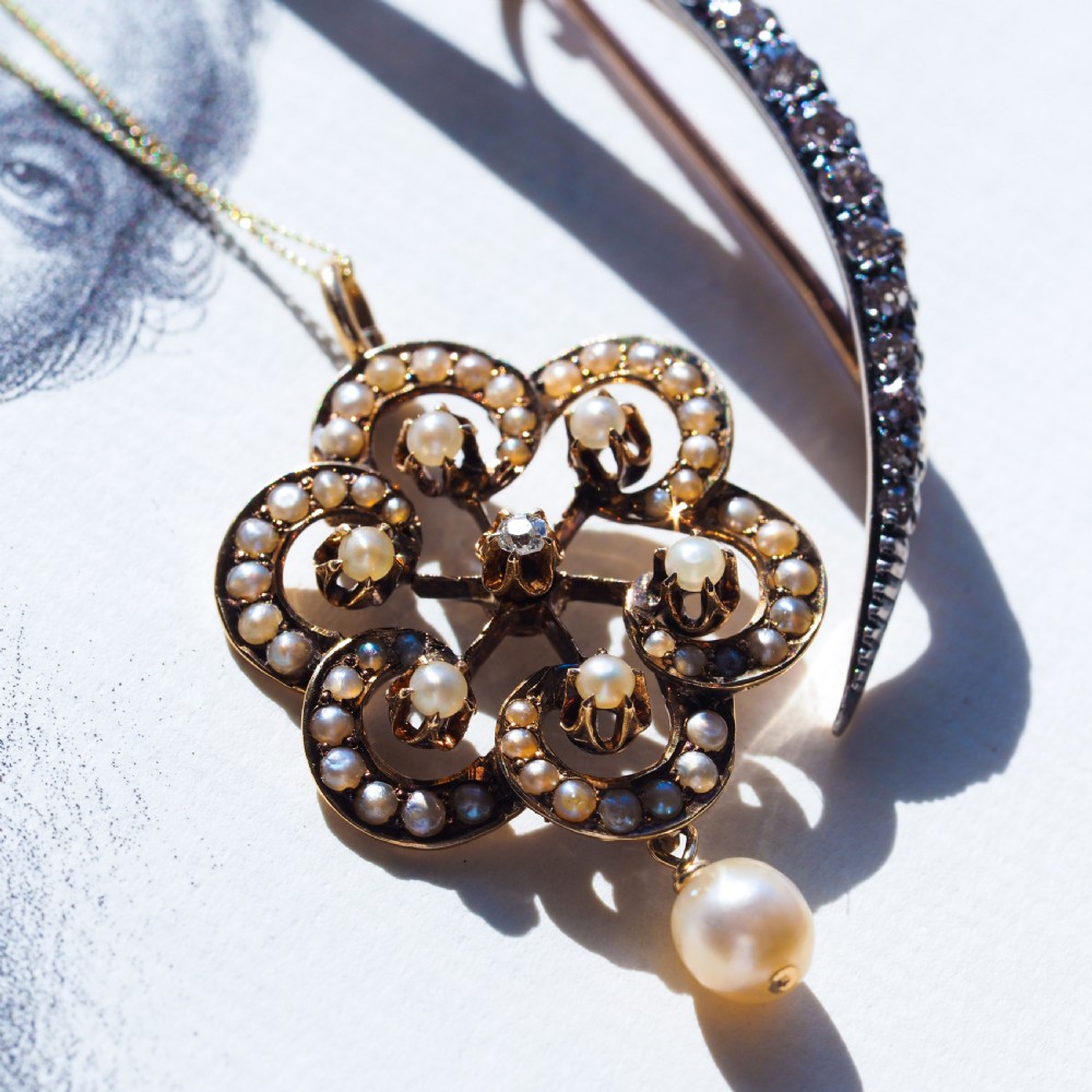 A Victorian 14ct yellow gold circular scrollwork pendant set with seed pearls, a central diamond, and an articulated pearl drop suspended from a fine chain. View XV