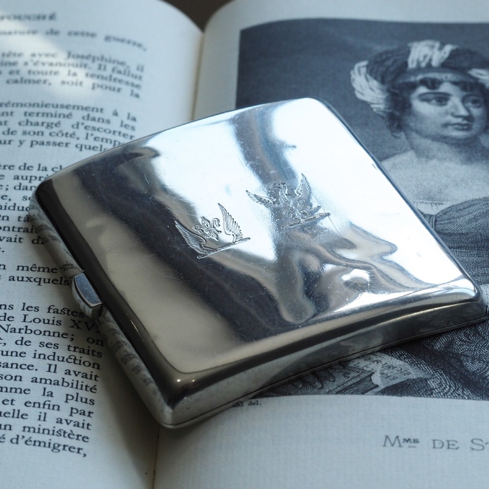 A polished Victorian sterling silver cigarette case featuring an engraved heraldic crest and curved profile resting on an open book.