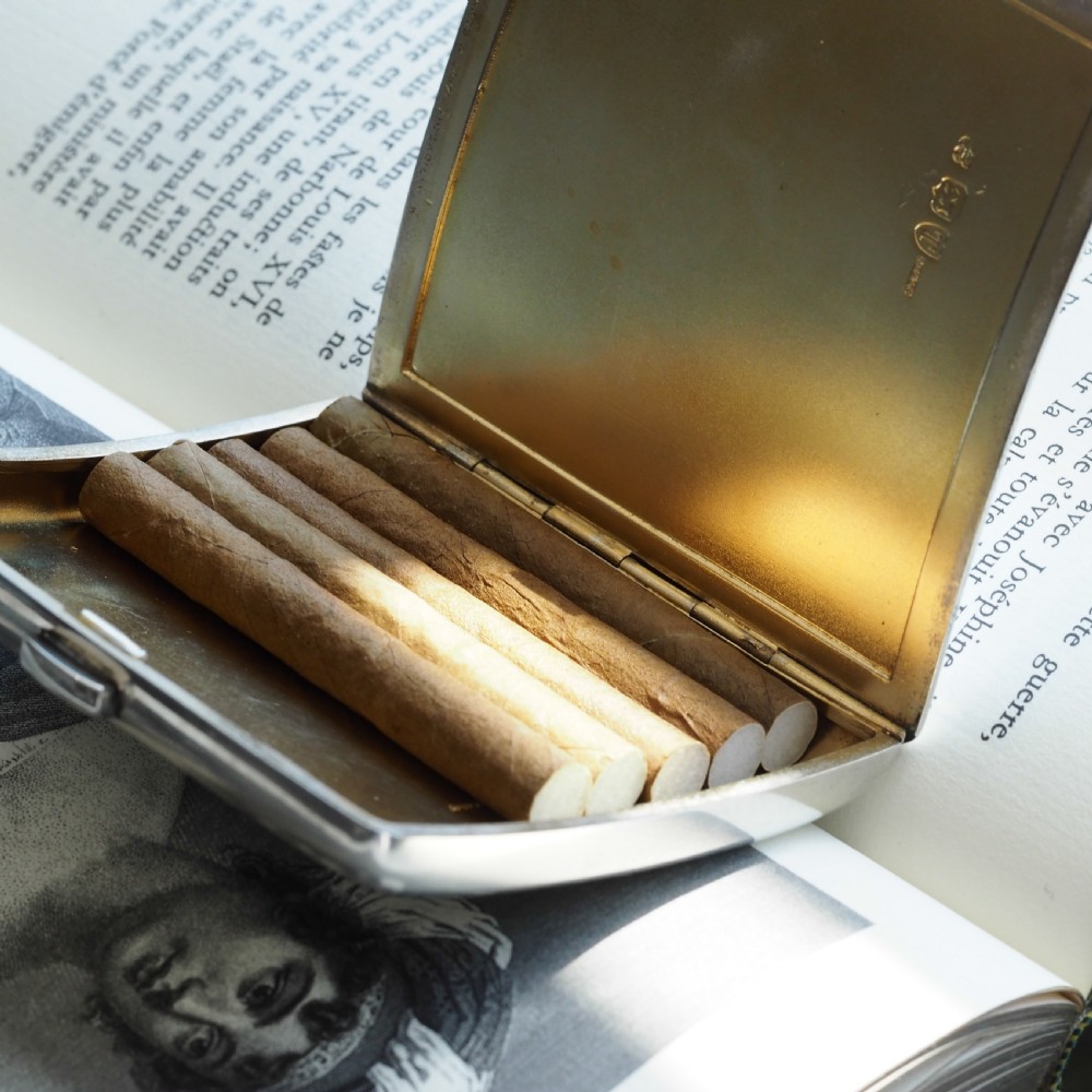 A polished Victorian sterling silver cigarette case featuring an engraved heraldic crest and curved profile resting on an open book. View II