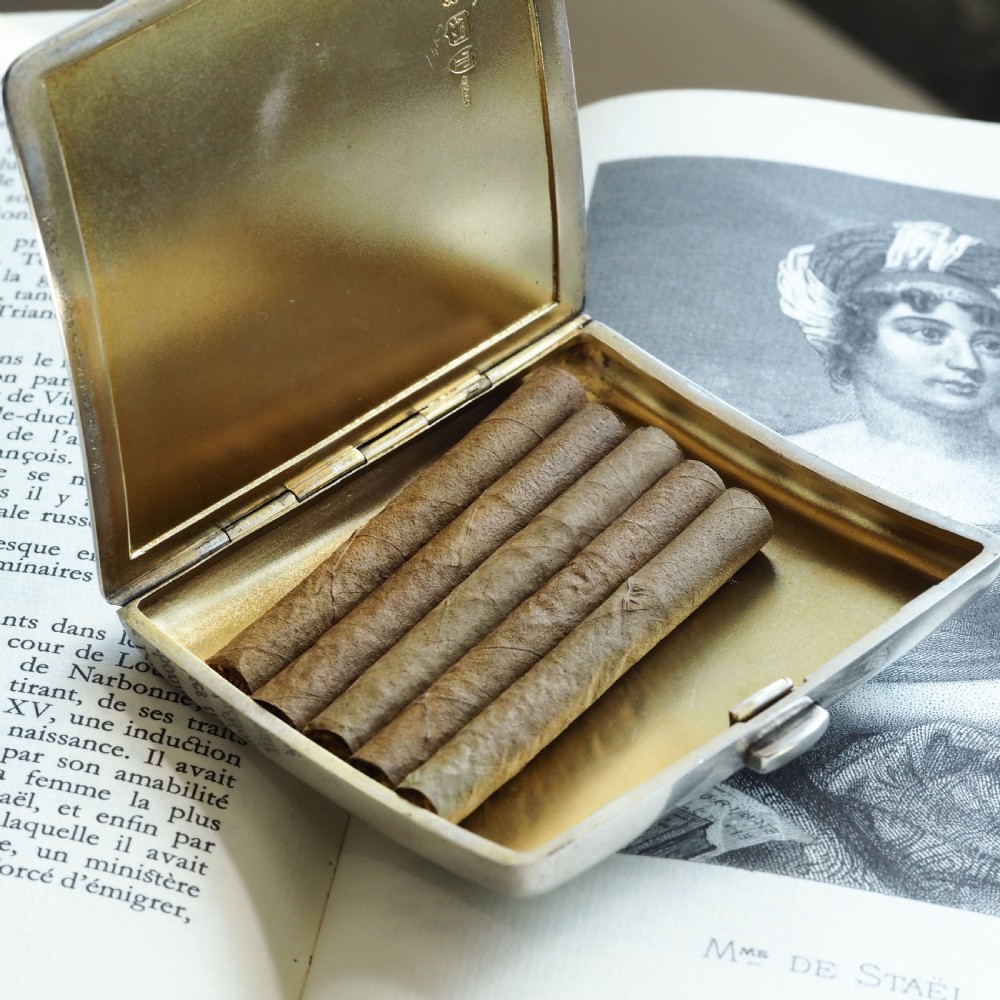 A polished Victorian sterling silver cigarette case featuring an engraved heraldic crest and curved profile resting on an open book. View III