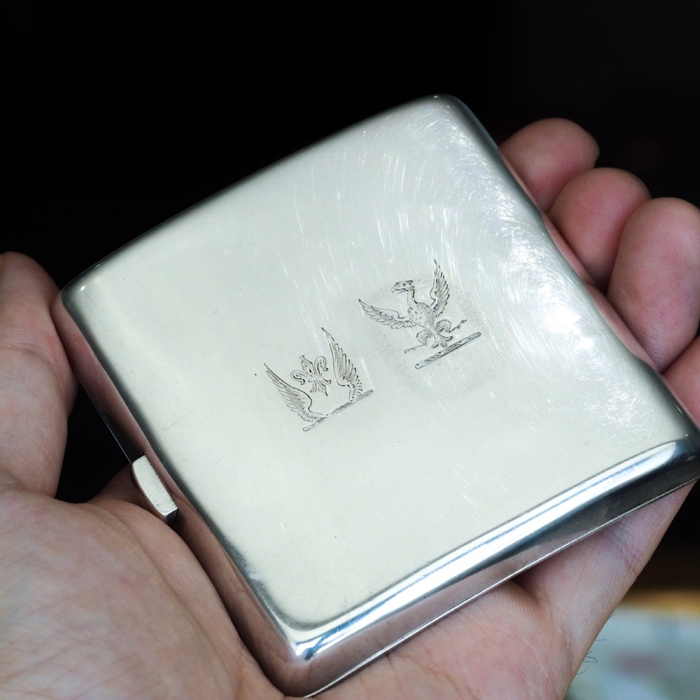 A polished Victorian sterling silver cigarette case featuring an engraved heraldic crest and curved profile resting on an open book. View V