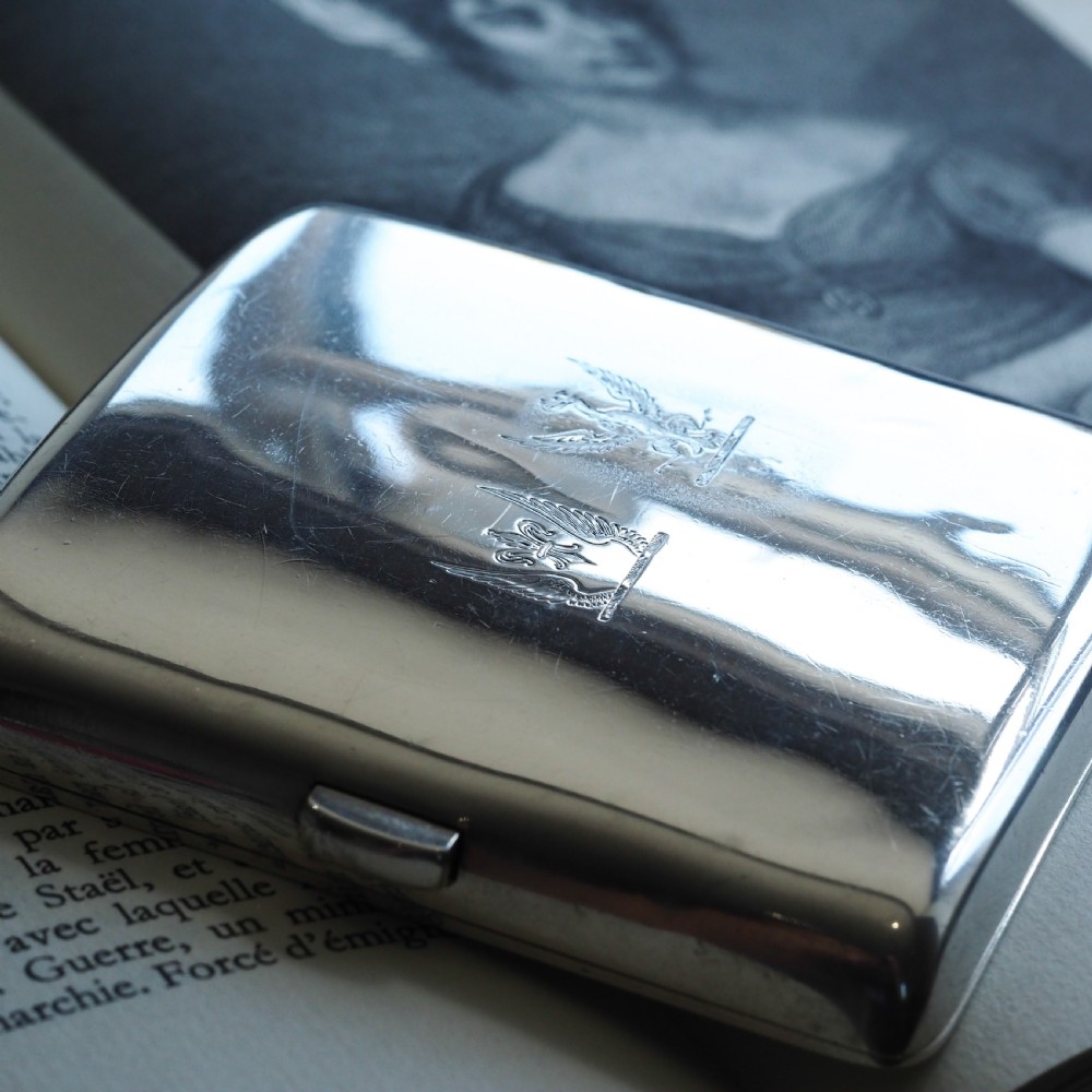 A polished Victorian sterling silver cigarette case featuring an engraved heraldic crest and curved profile resting on an open book. View VI