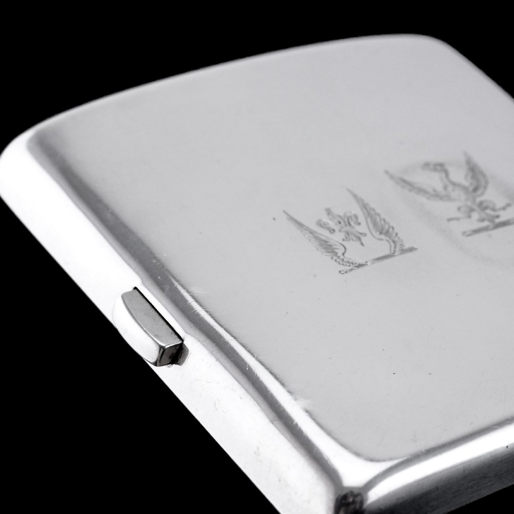 A polished Victorian sterling silver cigarette case featuring an engraved heraldic crest and curved profile resting on an open book. View IX