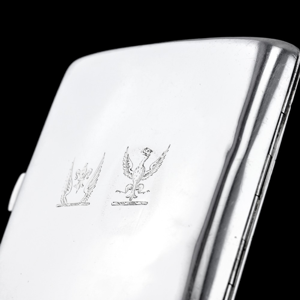 A polished Victorian sterling silver cigarette case featuring an engraved heraldic crest and curved profile resting on an open book. View X