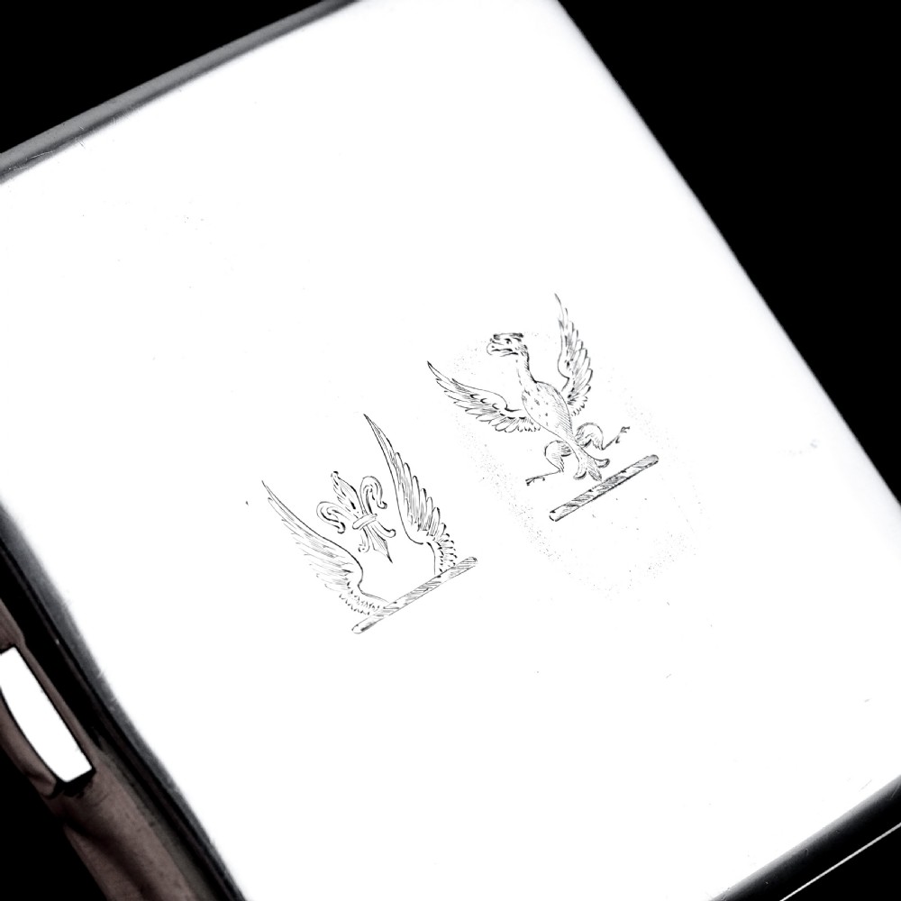 A polished Victorian sterling silver cigarette case featuring an engraved heraldic crest and curved profile resting on an open book. View XI