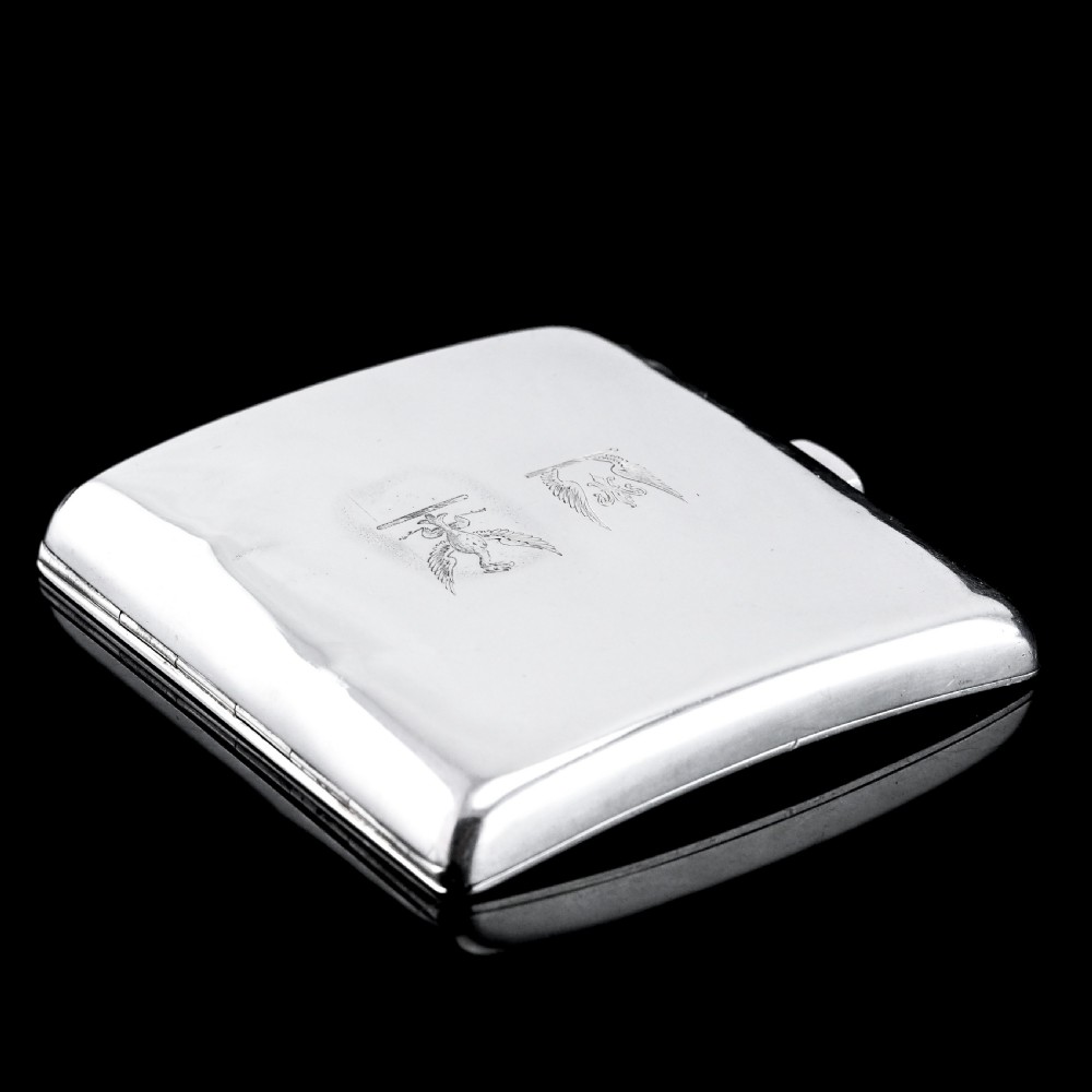 A polished Victorian sterling silver cigarette case featuring an engraved heraldic crest and curved profile resting on an open book. View XII
