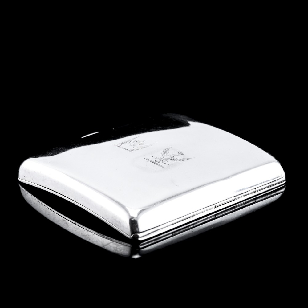 A polished Victorian sterling silver cigarette case featuring an engraved heraldic crest and curved profile resting on an open book. View XIII