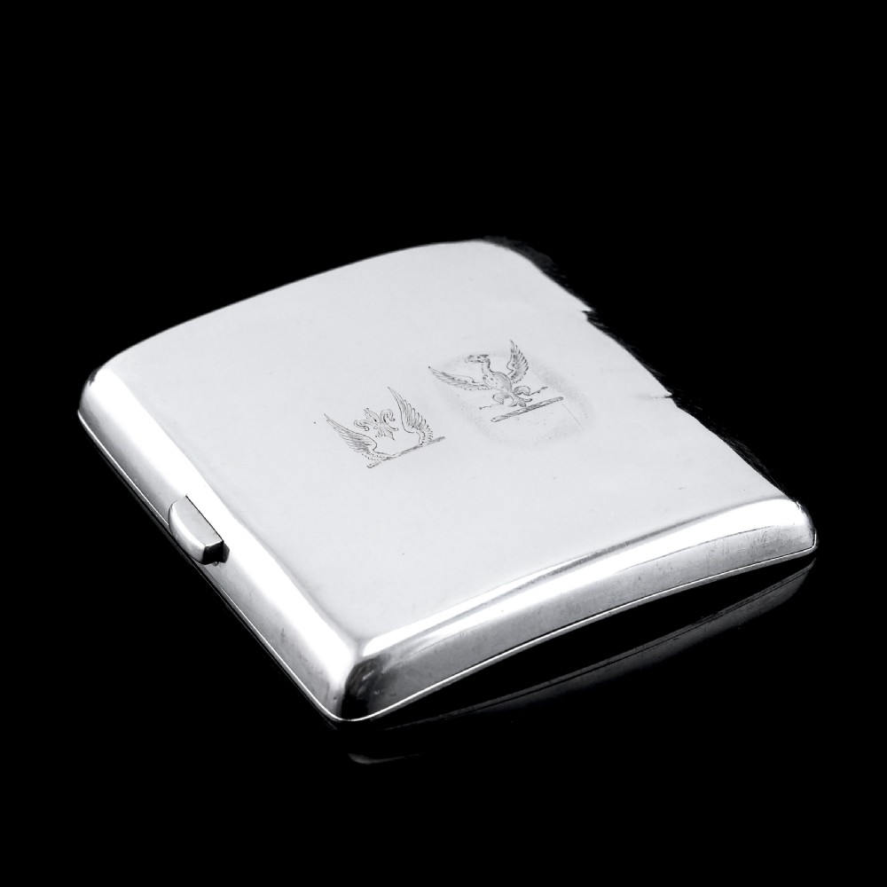 A polished Victorian sterling silver cigarette case featuring an engraved heraldic crest and curved profile resting on an open book. View XIV