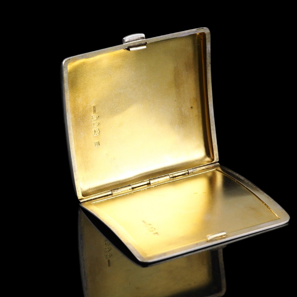 A polished Victorian sterling silver cigarette case featuring an engraved heraldic crest and curved profile resting on an open book. View XV