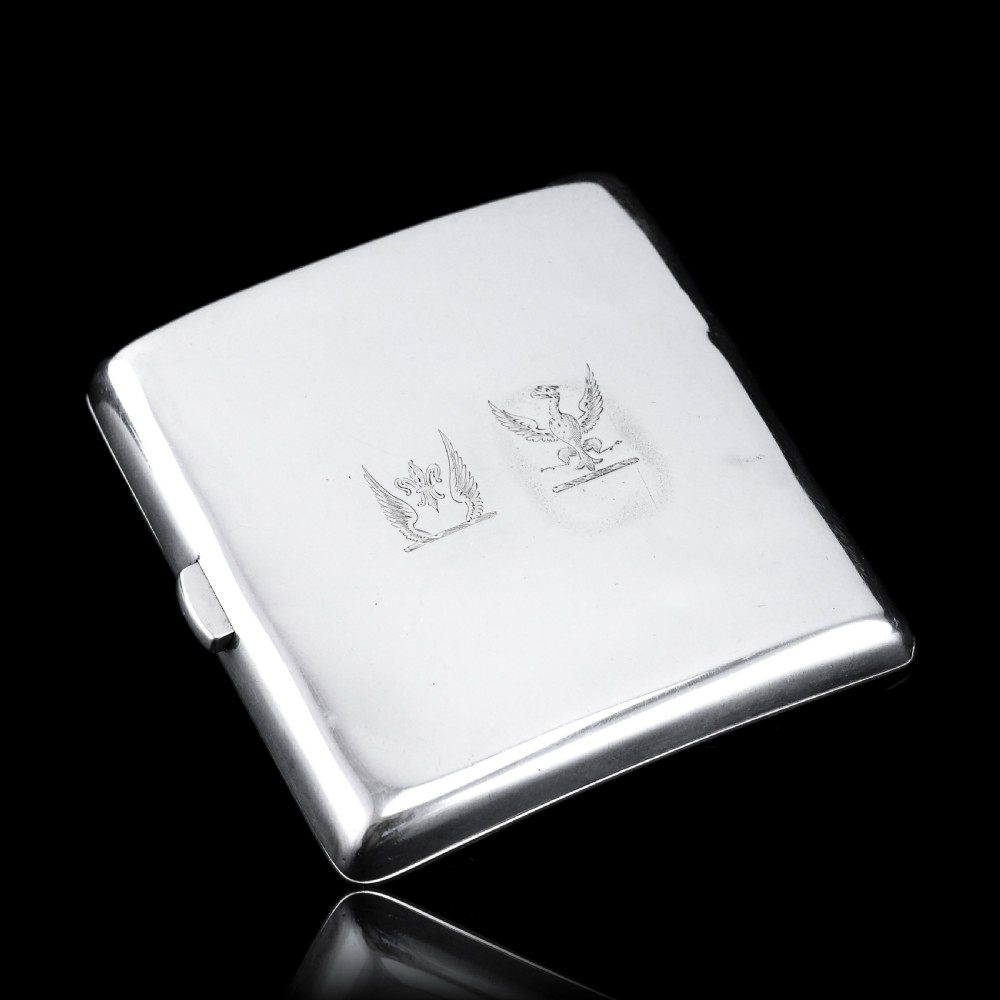 A polished Victorian sterling silver cigarette case featuring an engraved heraldic crest and curved profile resting on an open book. View XVII