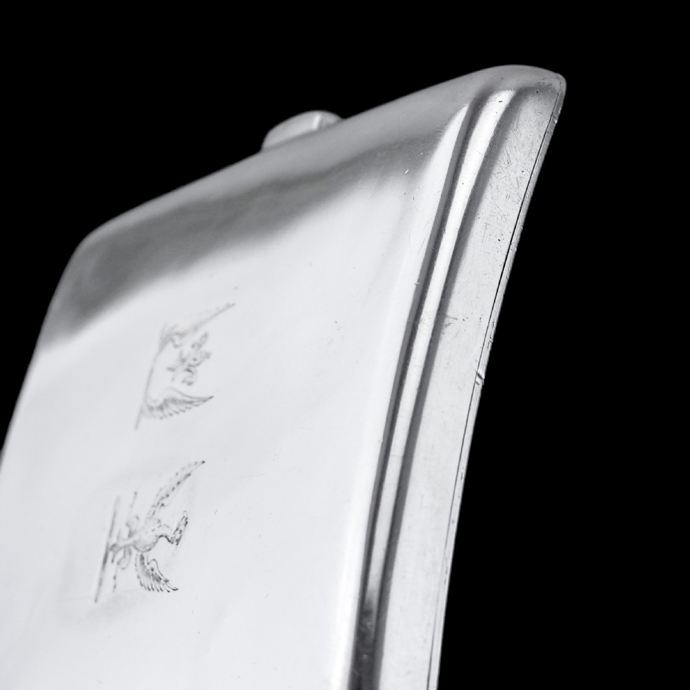 A polished Victorian sterling silver cigarette case featuring an engraved heraldic crest and curved profile resting on an open book. View XVIII