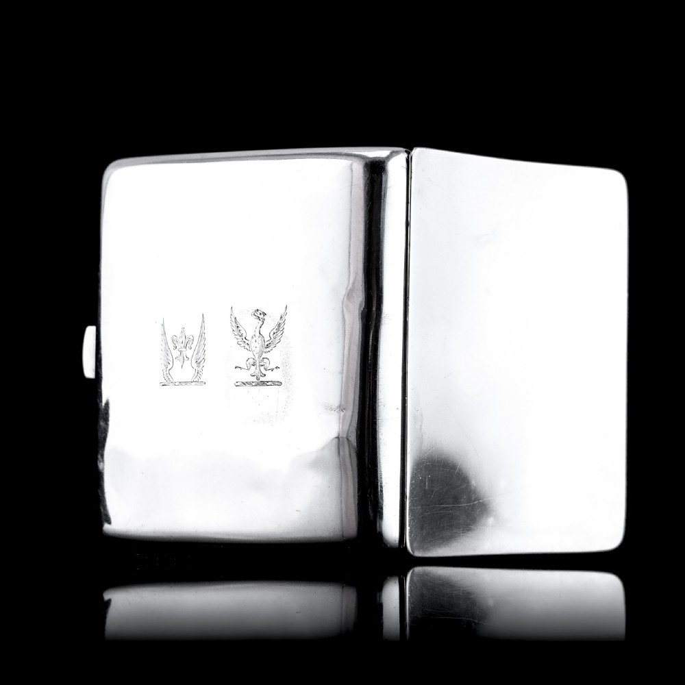 A polished Victorian sterling silver cigarette case featuring an engraved heraldic crest and curved profile resting on an open book. View XIX